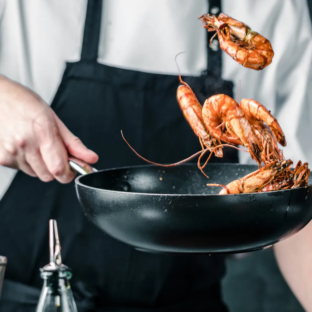 A person tosses seafood in a wok.
